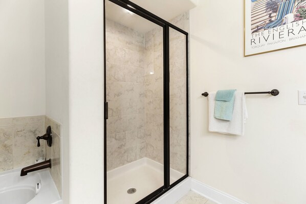 A bathroom with a glass-enclosed shower, a white bathtub, and a towel rack with a towel.