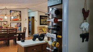 Ein Essbereich mit Holztisch und Stühlen, einer Kristallleuchter und einem an der Wand befestigten Weinkühlschrank mit Flaschen.