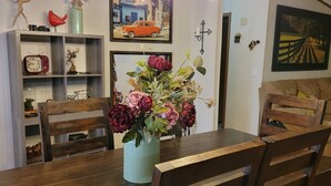 Ein Essbereich mit einem Holztisch, zwei Stühlen, einem Blumenstrauß und einem Regal mit verschiedenen Gegenständen, darunter eine Uhr und eine kleine Statue.