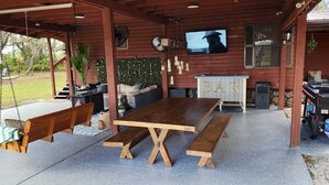 A covered outdoor area with a wooden table and benches, a bar area, and a television screen. - 10 Acres  Farm House (Frostproof)