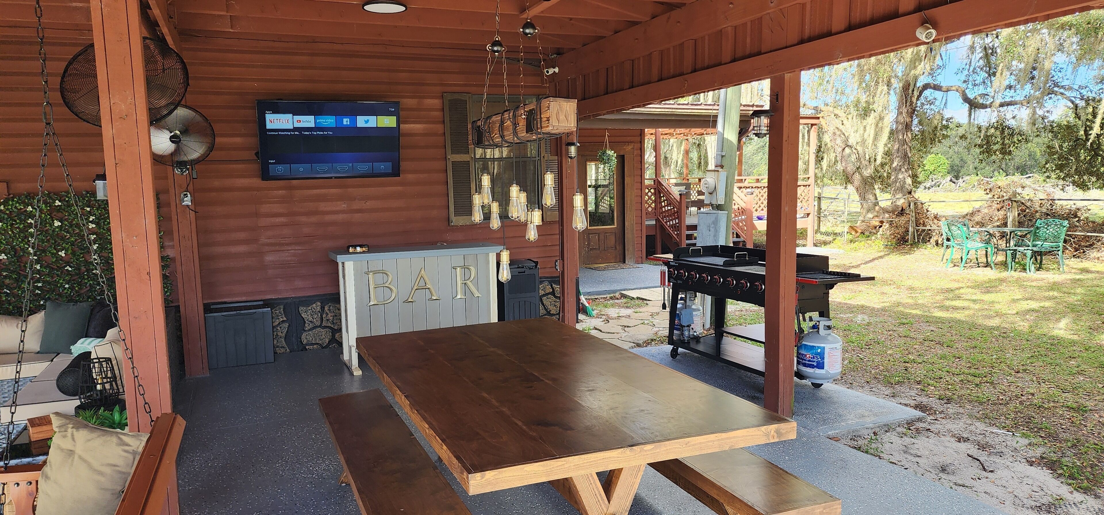 A wooden outdoor bar area with a TV displaying Netflix, a grill, and a swing chair.