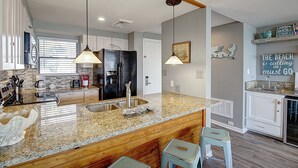 Una cocina moderna con encimeras de granito, electrodomésticos de acero inoxidable y una isla central con taburetes de bar.