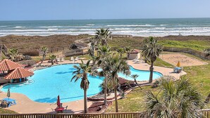 Zona de piscina con vista al océano, rodeada de palmeras y una terraza de madera.