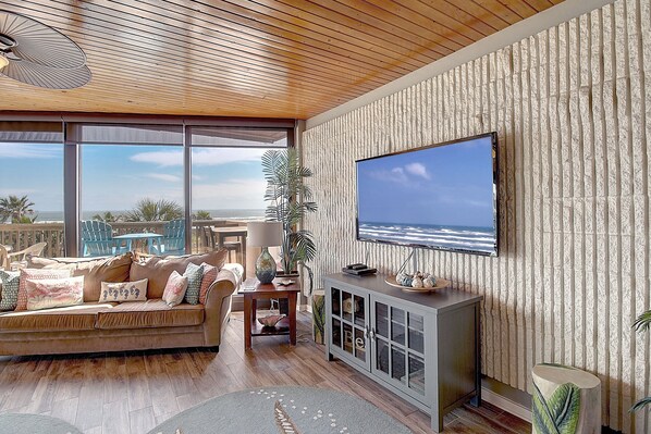 A living room with a large TV, wooden ceiling, and a view of the ocean. - Mayan Princess 314 | Panoramic Ocean-Pool Views (Port Aransas)