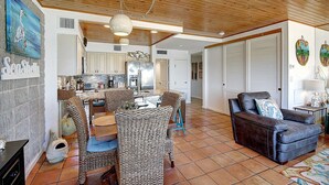 A spacious living area with a dining table, comfortable seating, a kitchen in the background, and a cozy fireplace. - Easy pool and beach access | MP 114 (Port Aransas)