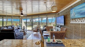A spacious living area with a large TV, comfortable seating, a kitchen counter, and a view of the outdoors. - Easy pool and beach access | MP 114 (Port Aransas)
