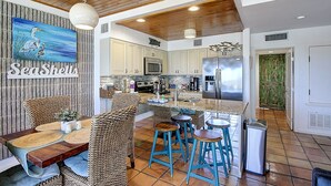 A spacious kitchen with white cabinets, a large island, and blue bar stools. - Easy pool and beach access | MP 114 (Port Aransas)