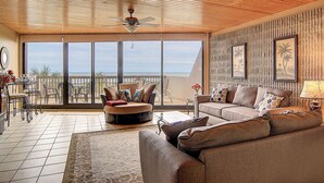 A spacious living area with a large window overlooking the beach, a ceiling fan, and a cozy seating arrangement. - Ocean-Pool Views From 2 Balconies | MP315 (Port Aransas)