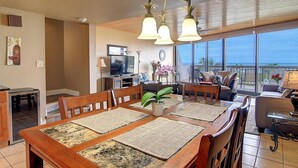 A spacious living area with a large dining table, comfortable seating, a television, and a balcony with a view. - Ocean-Pool Views From 2 Balconies | MP315 (Port Aransas)