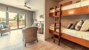 A room with a bunk bed, wicker furniture, a ceiling fan, and a view through large windows.