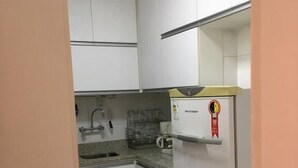 Une cuisine de taille réduite avec des meubles blancs, un évier en acier inoxydable et un réfrigérateur orné d’un logo rouge.