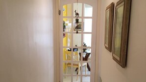Un couloir carrelé mène à une pièce dotée d’une porte. Deux tableaux encadrés ornent le mur, à droite.