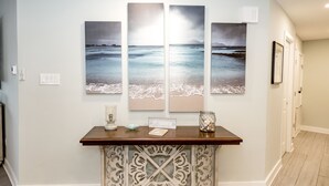 A hallway with a wooden console table, a framed beach artwork, and a decorative wall piece.