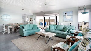 A spacious living room with teal sofas, a wooden coffee table, and a large clock on the wall.