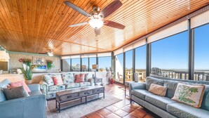 A spacious living area with a high ceiling, large windows, and a ceiling fan.