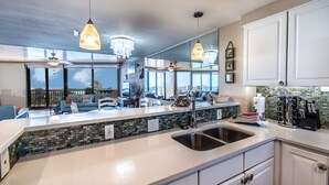A modern kitchen with a large island, granite countertops, and pendant lighting.