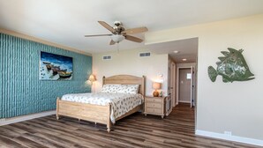 A bedroom with a wooden bed, a ceiling fan, a nightstand with a lamp, and a wall-mounted fish decoration.