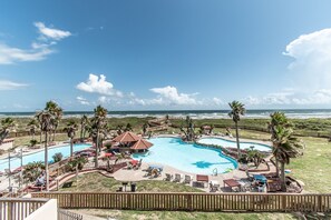 A resort with a large swimming pool, palm trees, and a view of the ocean.