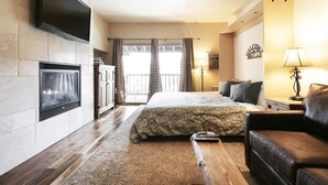Ein Hotelzimmer mit Kamin, einem Bett mit gemustertem Überwurf, einem Ledersofa, einem an der Wand montierten Fernseher und einem Balkon mit Vorhängen.