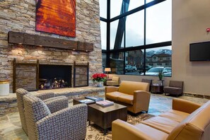 Un hall con chimenea de piedra, sofás de cuero, un televisor de pantalla plana y un amplio ventanal con vistas al exterior.