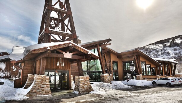 Eine Holzhütte mit einem hohen Holzturm, Steinsäulen und einem Parkplatz mit Autos.
