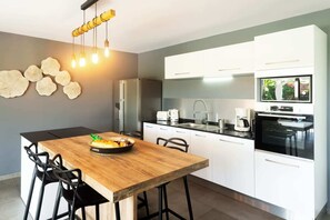 A modern kitchen with a wooden dining table, white cabinets, and a built-in oven. - Villa La Perle with private pool (GOSIER)