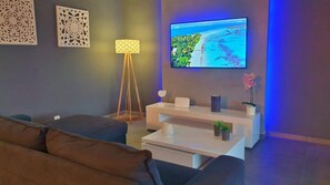 A modern living room with a flat-screen TV mounted on the wall, a white coffee table, a brown sofa, and decorative wall art. - Villa La Perle with private pool (GOSIER)