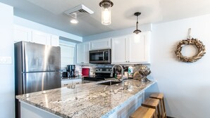A modern kitchen with a granite island, stainless steel appliances, and a pendant light.