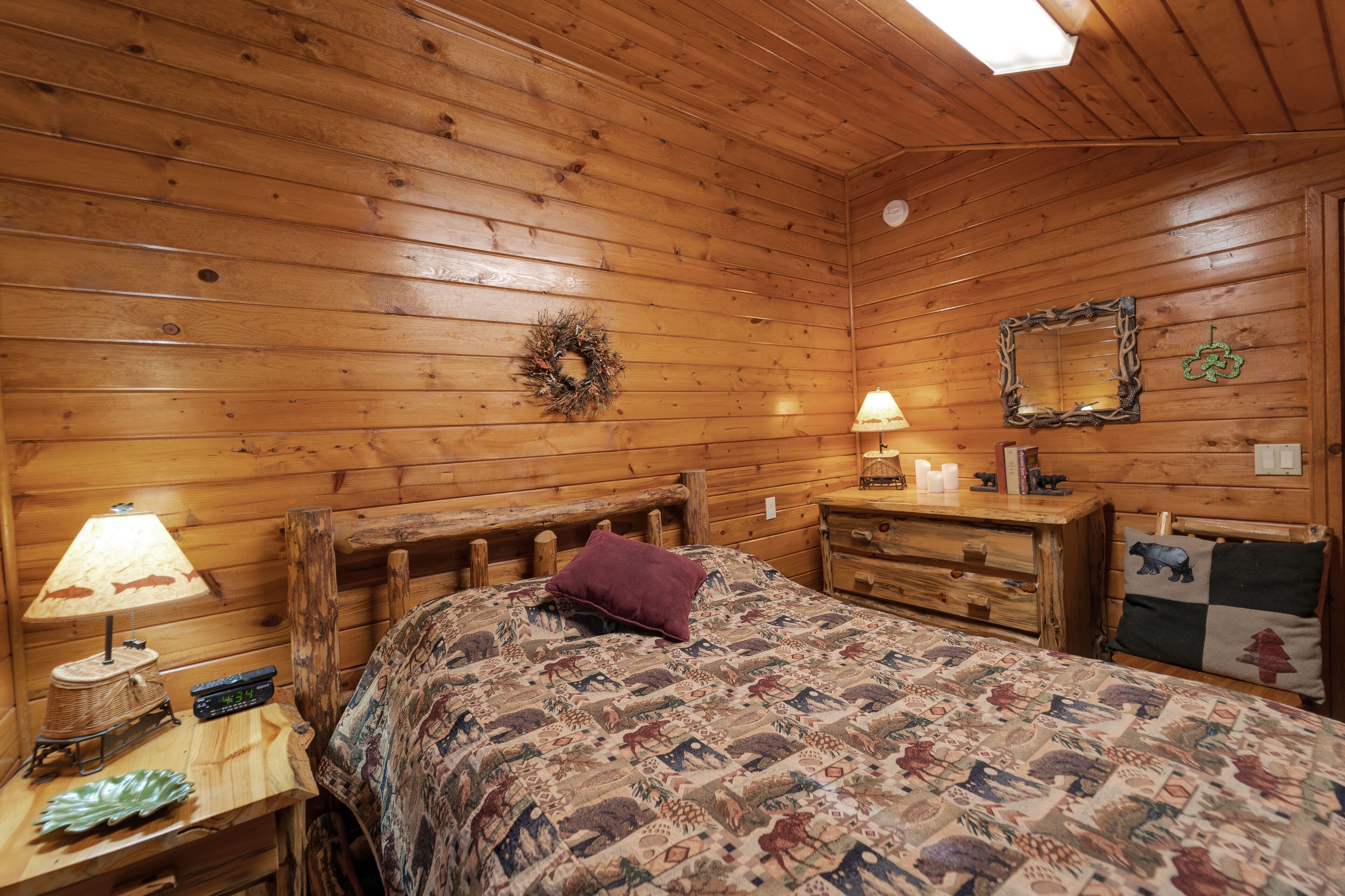Ein Schlafzimmer einer Holzhütte mit einem Bett, einem Nachttisch, einer Kommode und einer Lampe.