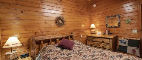 Ein Schlafzimmer einer Holzhütte mit einem Bett, einem Nachttisch, einer Kommode und einer Lampe.