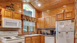 A kitchen with wooden cabinets, a white stove, a microwave, and a refrigerator. - Wisc Dells Amish Cabin in Woods for 10 people (Wisconsin Dells)