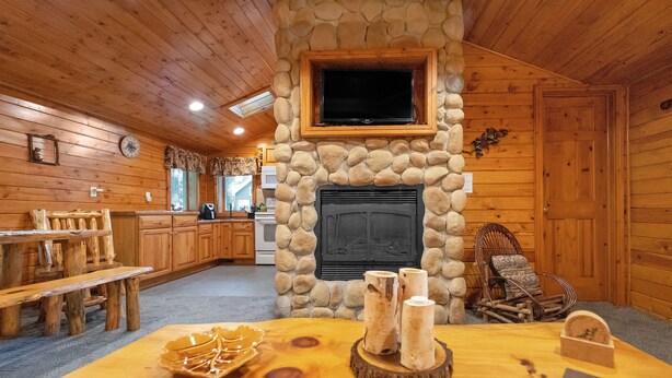 A cozy cabin interior with a stone fireplace, wooden furniture, and a television mounted above it. - Wisc Dells Amish Cabin in Woods for 10 people (Wisconsin Dells)