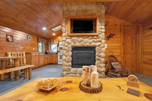 A cozy cabin interior with a stone fireplace, wooden furniture, and a television mounted above it. - Wisc Dells Amish Cabin in Woods for 10 people (Wisconsin Dells)