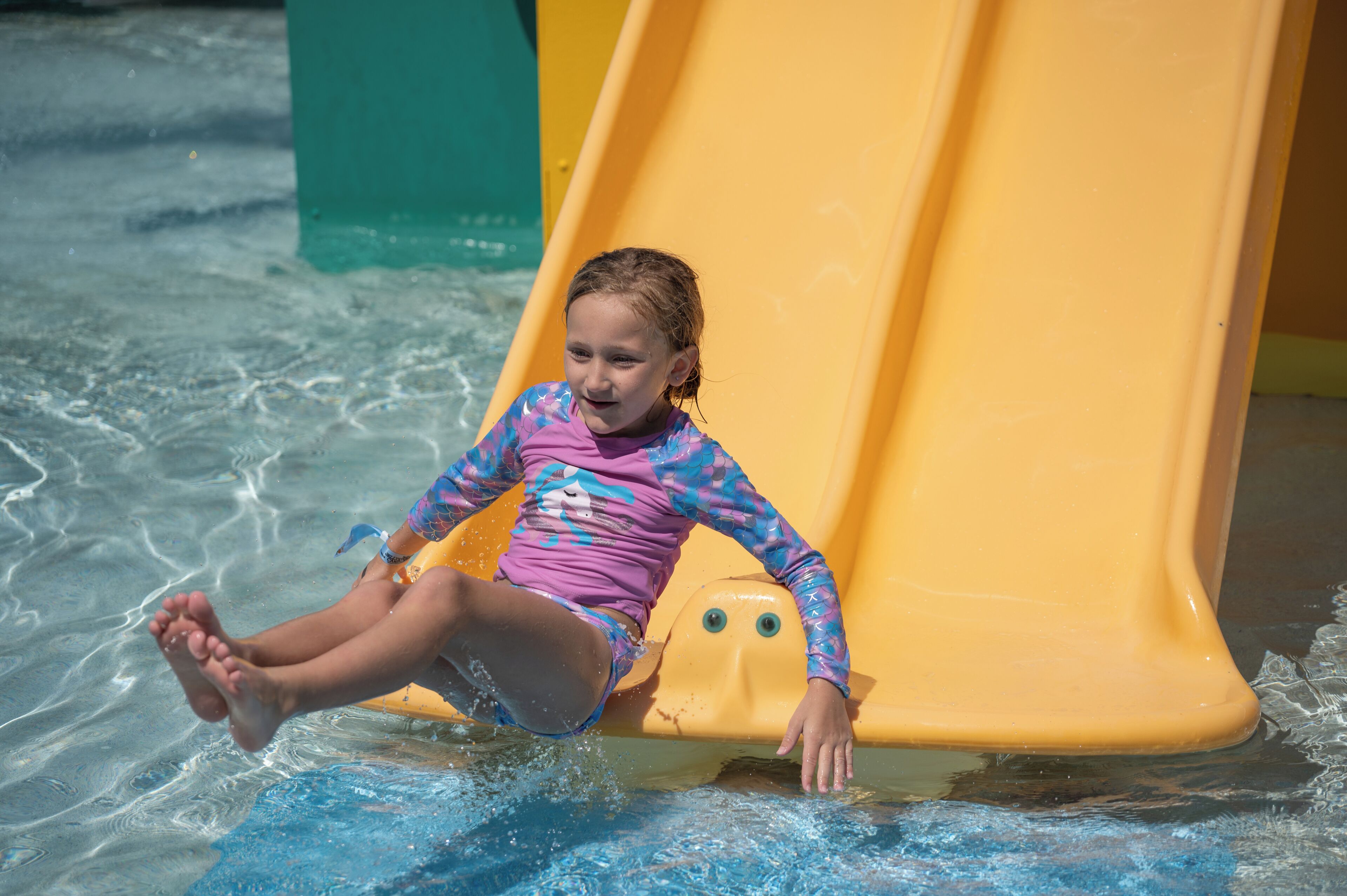 A child sliding down a yellow slide in a water park.
