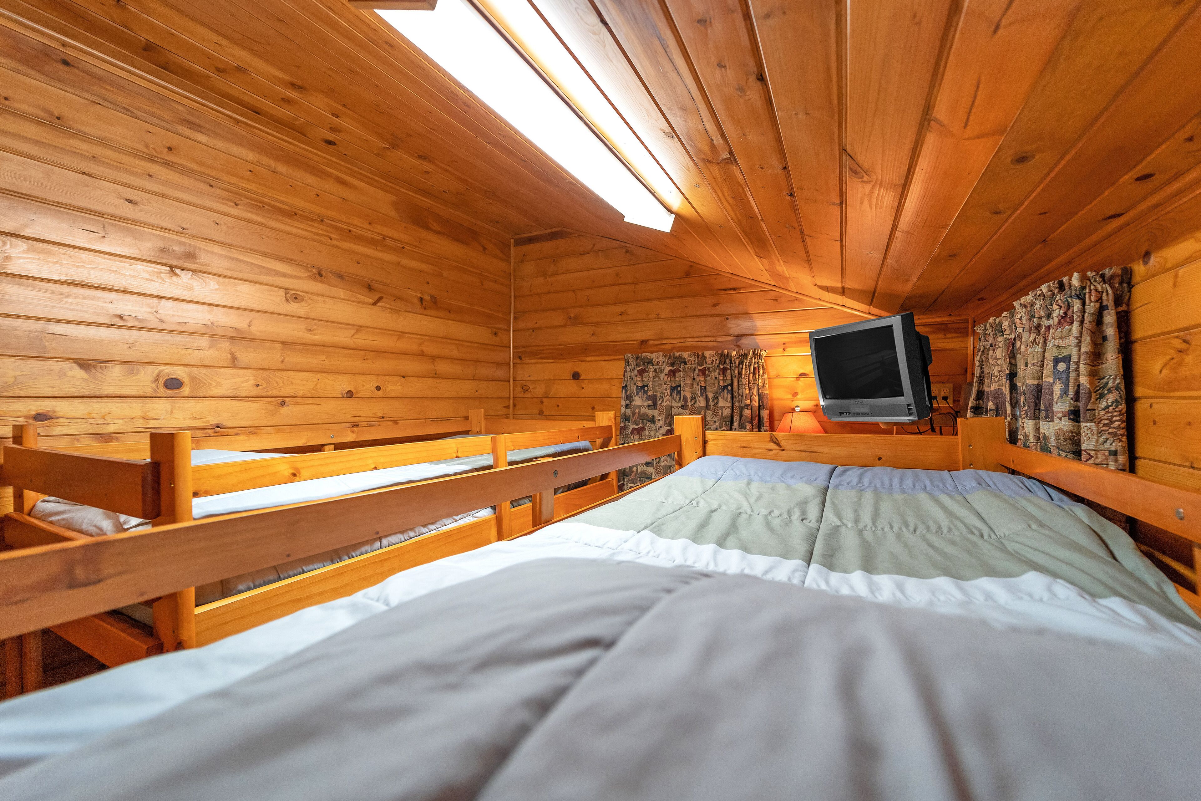 Una habitación de cabaña de madera con literas, un televisor y una ventana con cortinas.
