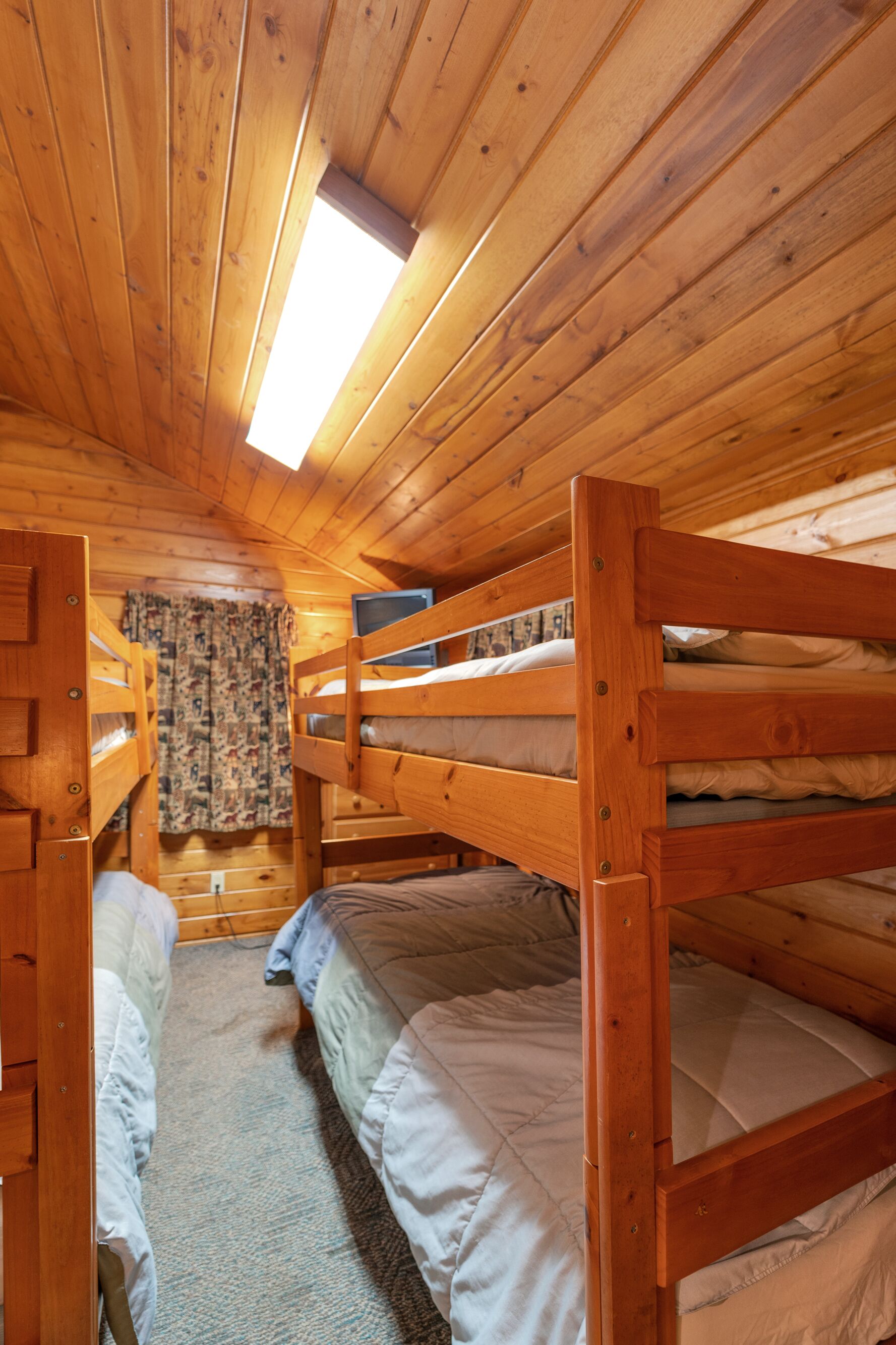 Une cabane en bois avec des lits superposés, une petite fenêtre et un rideau à motifs.