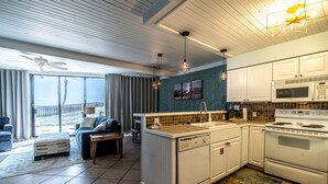 A modern kitchen with white cabinets, a built-in oven, and a microwave. There is a dining area with a table and chairs, and a large window offering a view of the outdoors. - Sassy Seagull @ The Mayan Princess (Port Aransas)