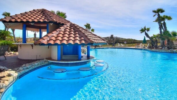 A swimming pool with a small structure featuring a tiled roof and a blue door. - Poolside views | Private access to beach | Beachfront | MP103 (Port Aransas)