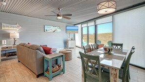 A spacious living area with a sofa, dining table, and chairs, a ceiling fan, and a TV. - A Beachy Dream MP118 | Resort Pools | Private Boardwalk (Port Aransas)