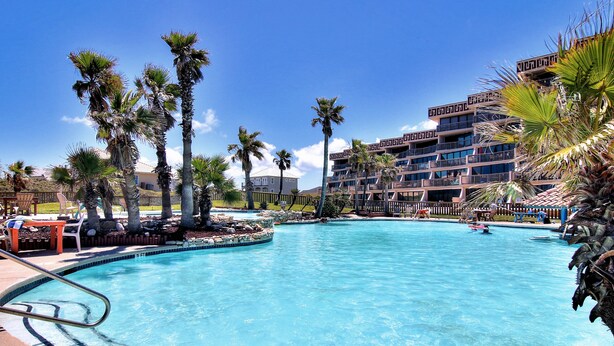 A swimming pool with a 3 ft no diving sign, surrounded by palm trees and a multi-story building with balconies. - A Beachy Dream MP118 | Resort Pools | Private Boardwalk (Port Aransas)