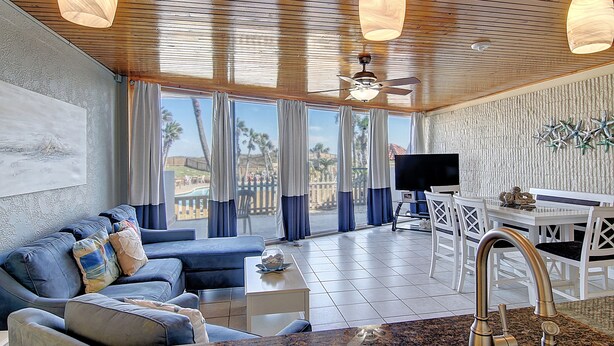 A living room with a sofa, a coffee table, and a TV. There is a dining area with a table and chairs. - Beachfront Vibes @ MP109 | Poolside Views | Beach Access (Port Aransas)