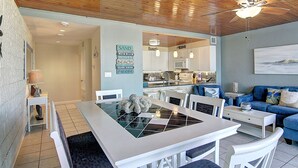 A modern kitchen with a microwave, sink, and dining area with a white table and chairs. - Beachfront Vibes @ MP109 | Poolside Views | Beach Access (Port Aransas)