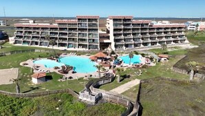 A large hotel with multiple balconies, two swimming pools, and a landscaped garden area. - Beachfront Vibes @ MP109 | Poolside Views | Beach Access (Port Aransas)