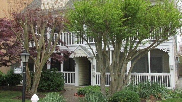 Una casa de dos pisos con un porche y un árbol en el jardín delantero.