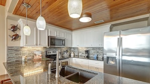 A modern kitchen with a granite countertop, stainless steel appliances, and a wooden ceiling.
