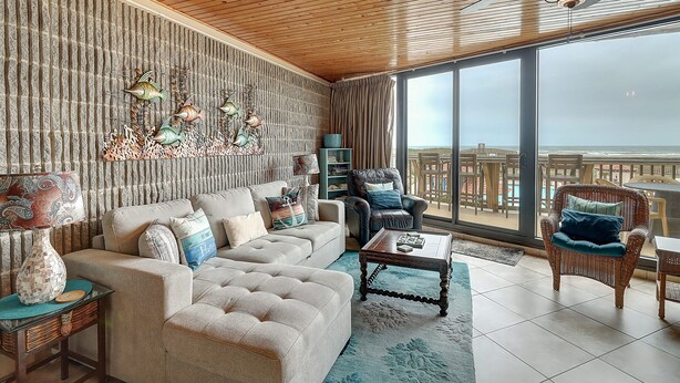 A spacious living room with a large window, a wooden ceiling, and a view of the ocean.