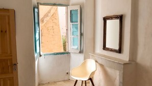 A bedroom with a bed, a chair, a window, and a mirror.