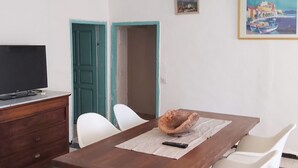 A dining area with a wooden table, white chairs, a bowl, and a remote control.