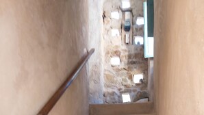 A staircase with stone walls and wooden handrails, leading to a room with a window and a door.