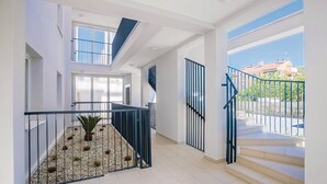 Um interior moderno com uma escada que leva a uma varanda, uma pequena área ajardinada e grandes janelas com vista para o exterior.
